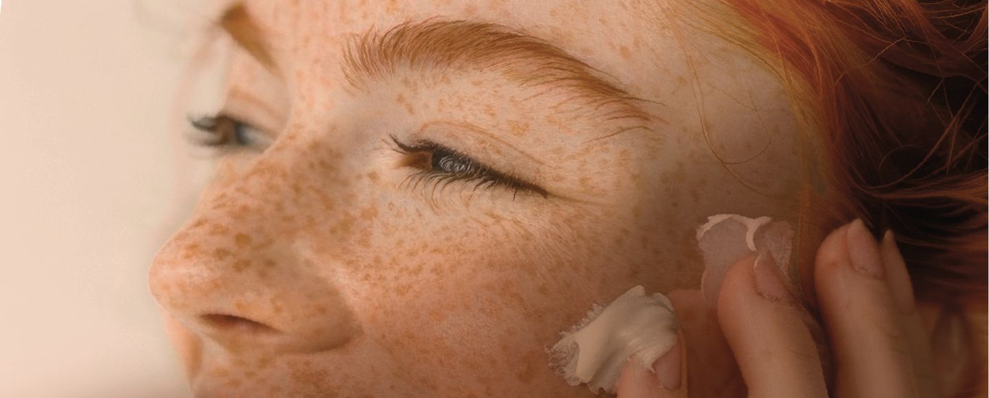 Le visage d'une jeune femme rousse appliquant une crème