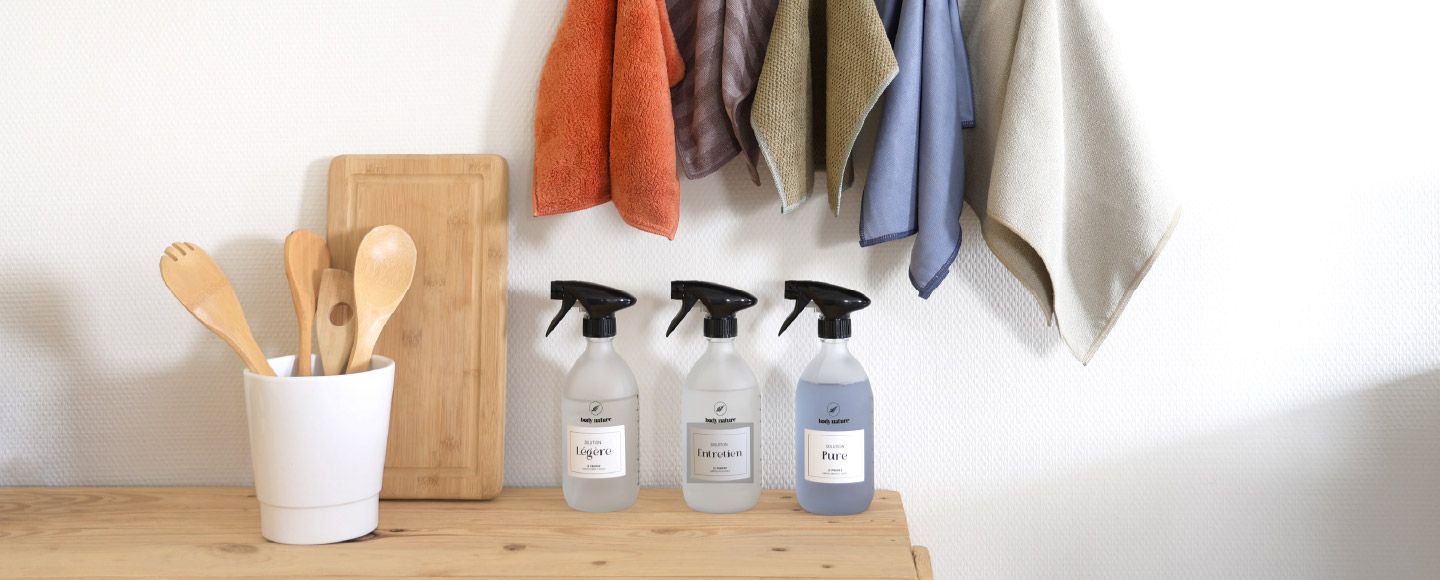 Les 3 flacons du propre poser sur un plan de travaille en bois avec les 5 microfibres accrochés