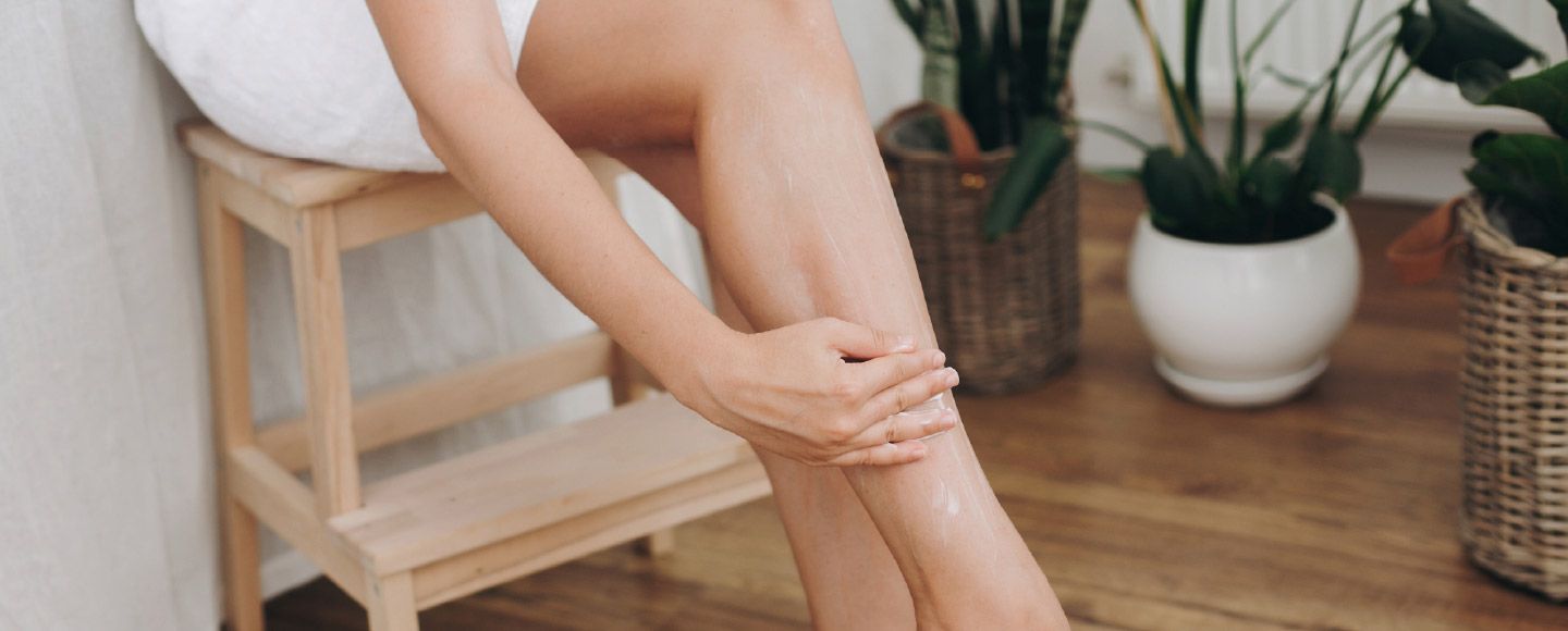 Une jeune femme qui s'applique de la crème sur les jambes assise sur une chaise en bois