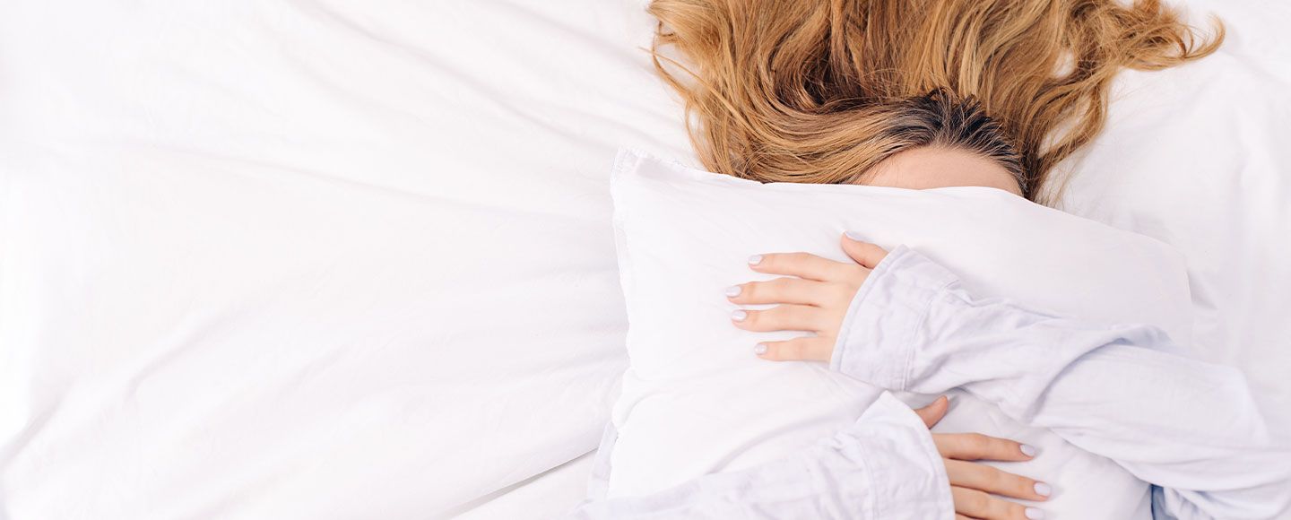 Une femme alongé sur un lit caché par une oreillé qu'elle sert dans ses bras