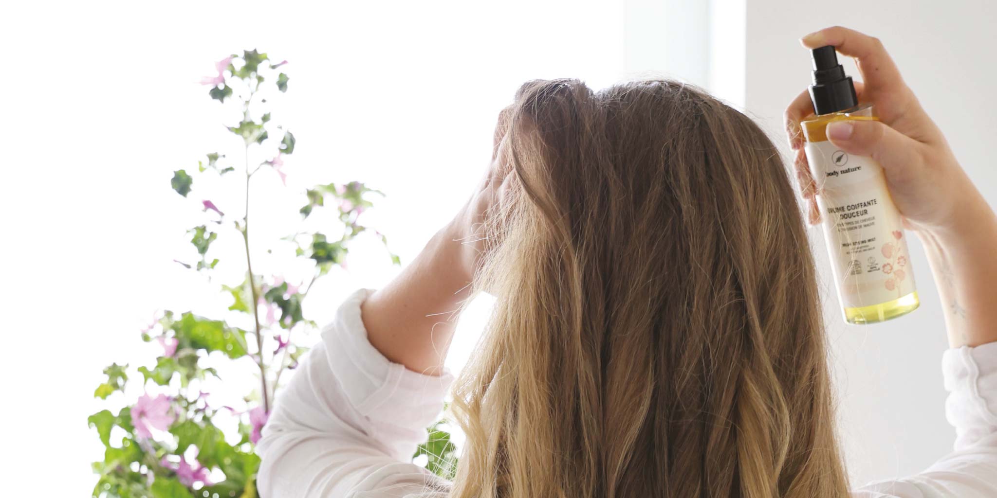 Une femme au long cheveux blond en train d'appliquer une brume pour cheveux