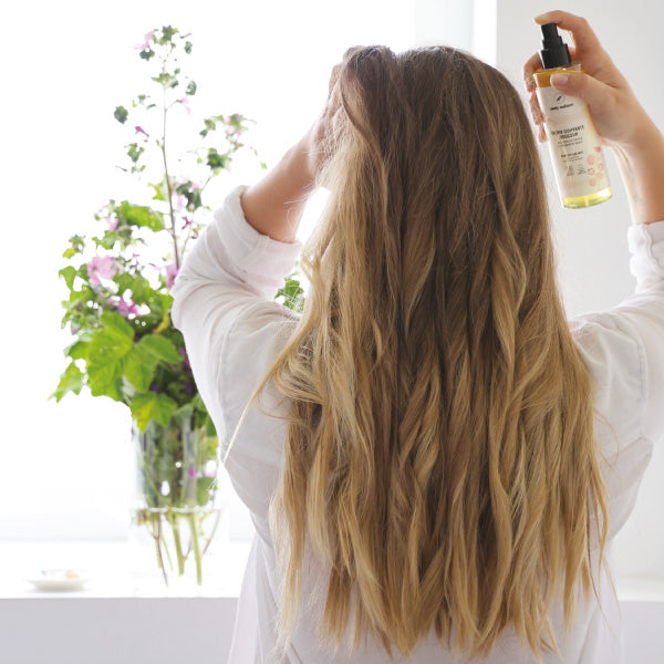 Une femme se met de la Brume coiffante douceur dans les cheveux