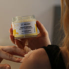 Pot d'un Soin après-soleil. Mise en scène : femme de dos, on ne voit que son épaule. Elle applique le Granité fraicheur sur son épaule avec une main. L'autre main tient le pot.