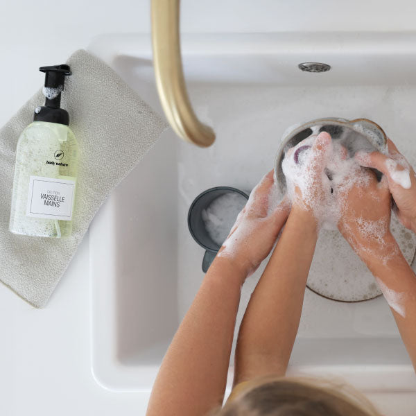 On voit les mains d'un enfant et sa maman en train de nettoyer la vaiselle avec le Vaisselle Mains Body Nature